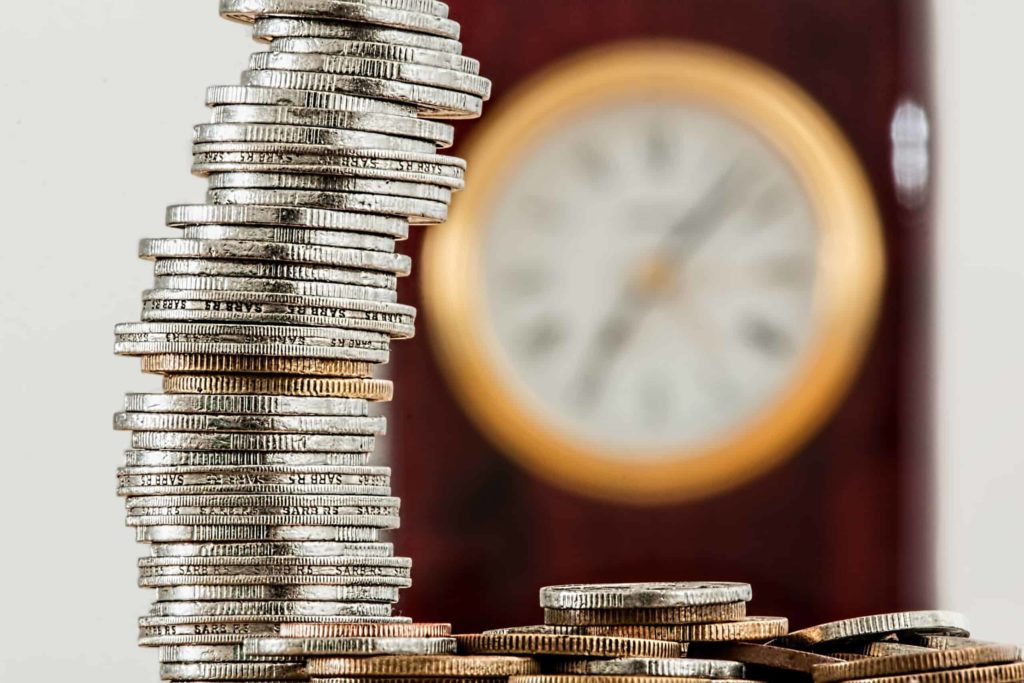 A stack of coins piled up in front of a blurred wall clock.