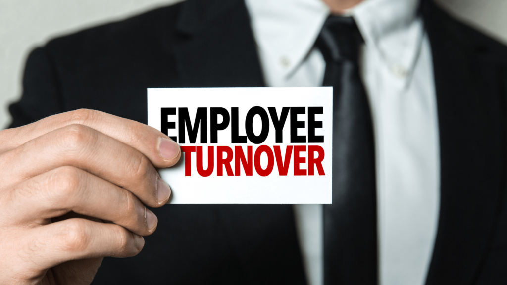 Man in a suit and tie holding up a white card that says "Employee Turnover" in black and red letters.